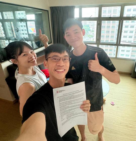 Wilfred with a young couple in their flat, holding the signed agreement